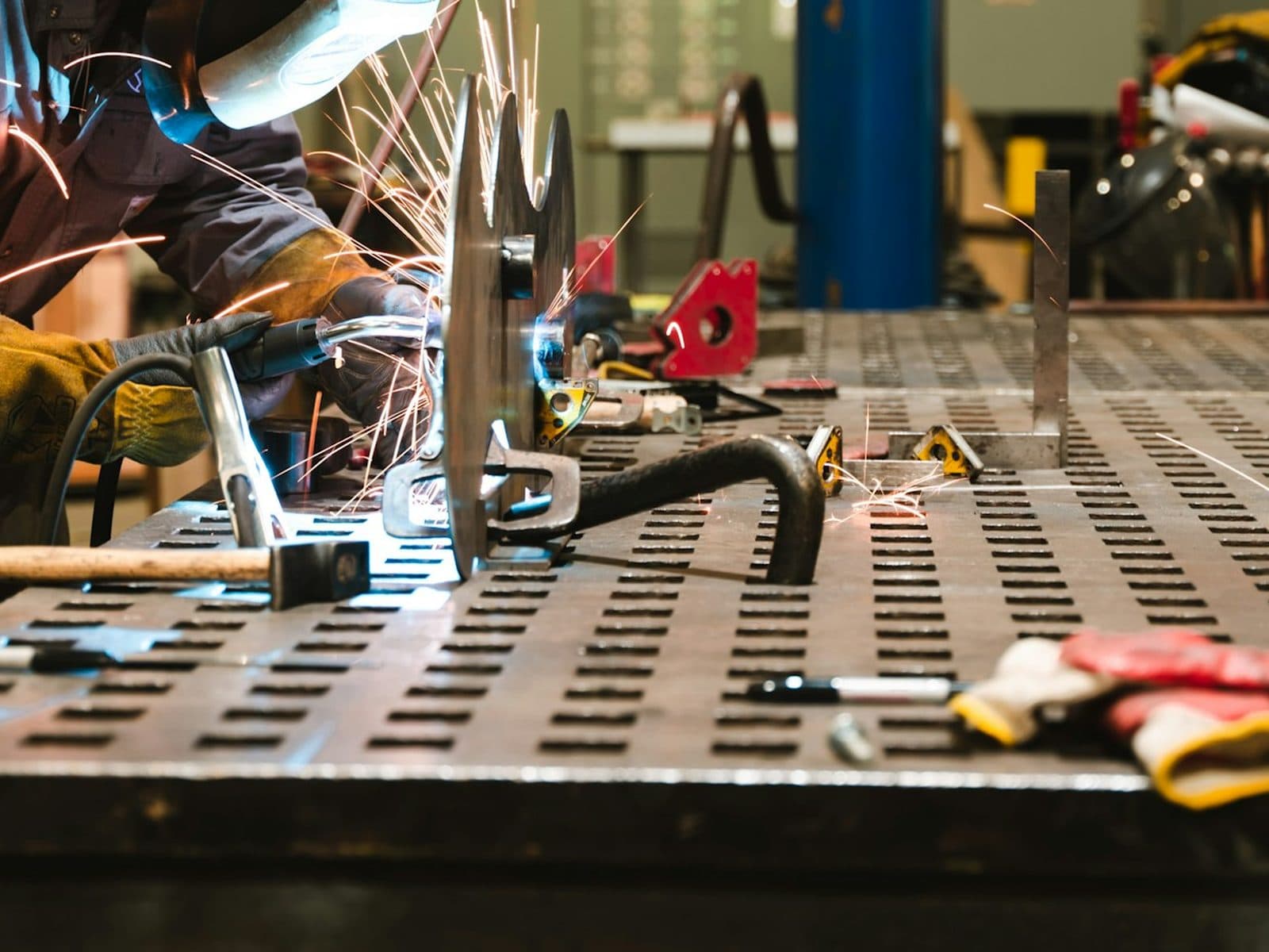 Hands welding a part on a steel fixture table in a fabrication shop